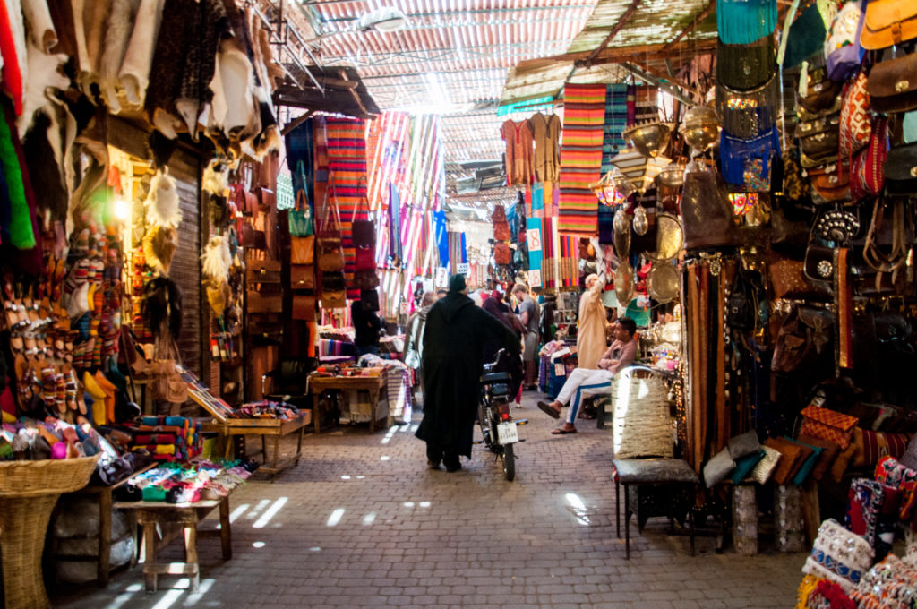 Bancarelle nell'ombreggiato suq di Marrakech, un uomo completamente coperto da una tunica passeggia tra schiere di bancarelle