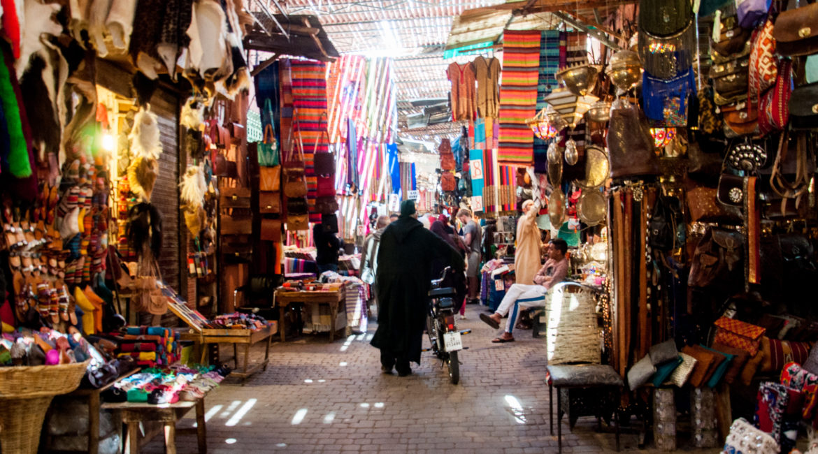 Bancarelle nell'ombreggiato suq di Marrakech, un uomo completamente coperto da una tunica passeggia tra schiere di bancarelle